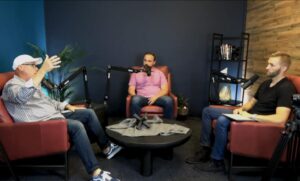 Three professionals recording a podcast conversation in a studio with microphones and cameras.