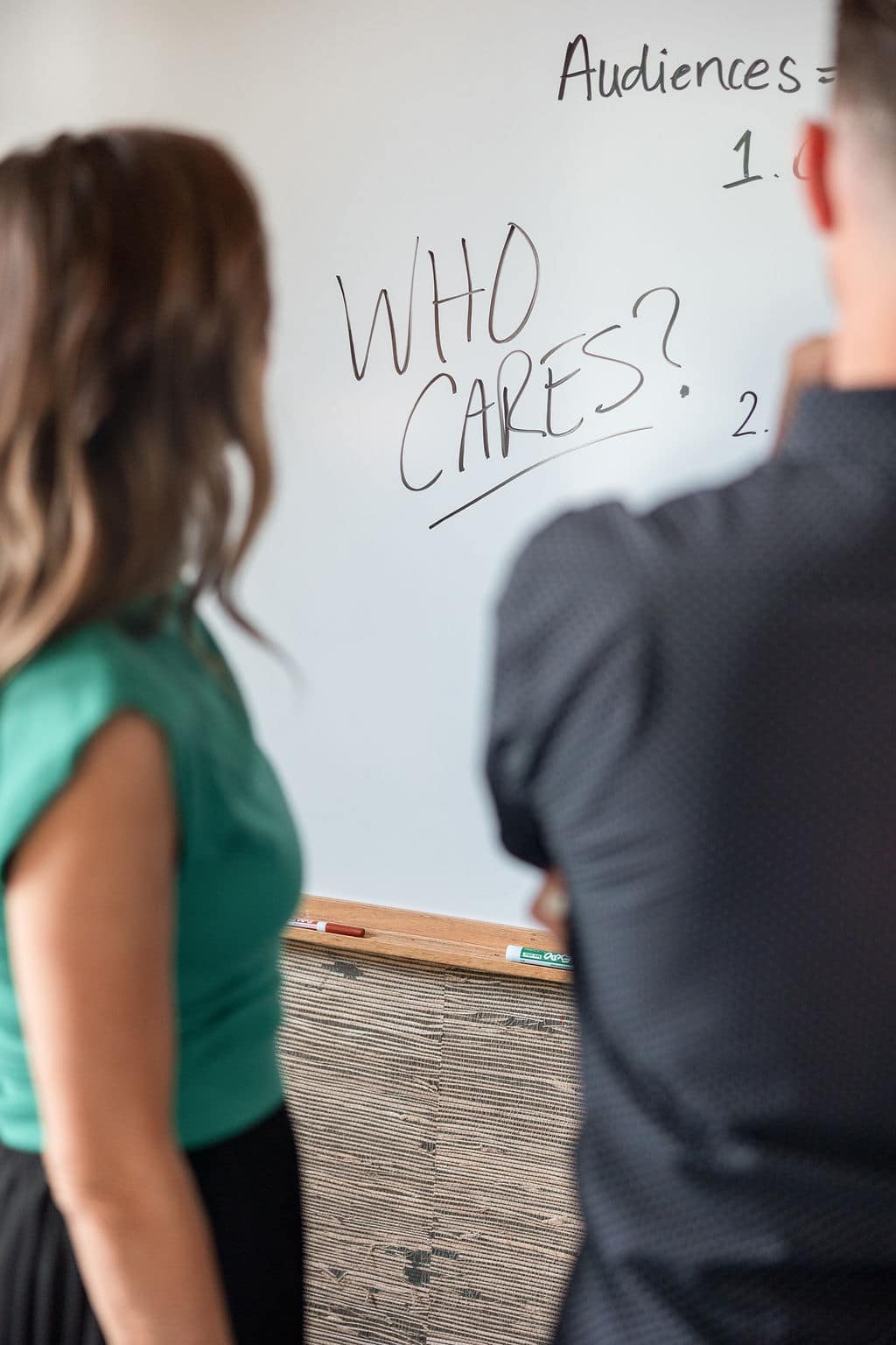 Two people reviewing a whiteboard with the words “Who Cares?” written in bold marker during a brand strategy session.