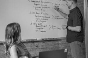 Man leading strategic whiteboard session while woman observes, defining key audience segments.