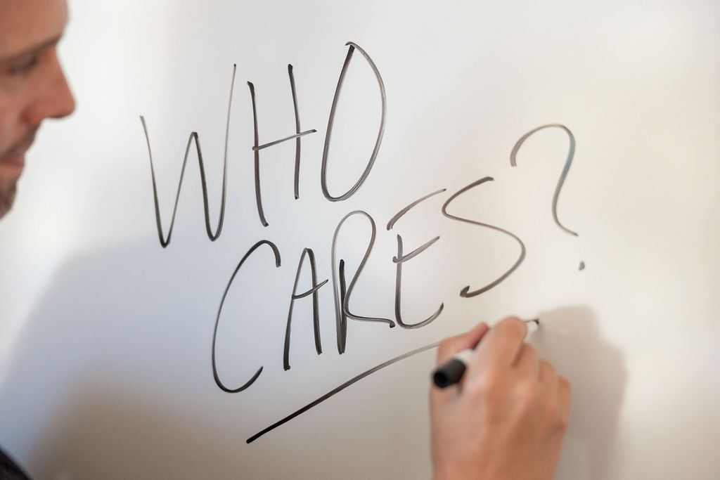 Person writing “WHO CARES?” on a whiteboard during a marketing strategy discussion.