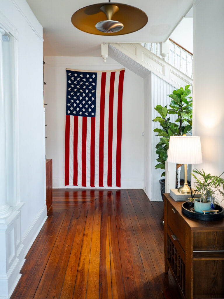 American flag hanging in the lobby of the Heritage Brands office with hardwood floors, staircase, and indoor plants.
